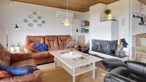 En hyggelig stue med lædersofaer, et sofabord i midten, en pejs og en hvid murstensvæg.