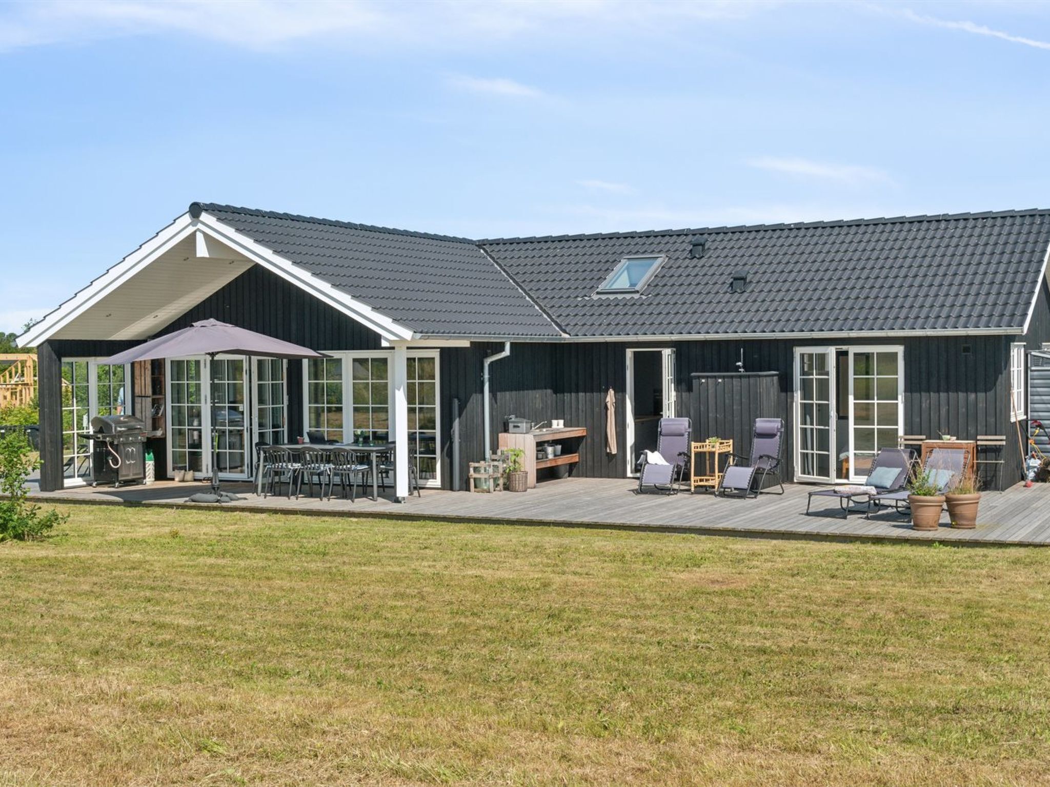 Een modern huis met een ruim terras, buitenmeubilair en een barbecuehoek.