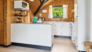Cocina compacta con paredes de madera, una isla central, un microondas y un ventanal con cortinas.