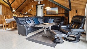Una sala de estar acogedora con un sofá de cuero, una mesa de comedor y un techo alto con vigas de madera.