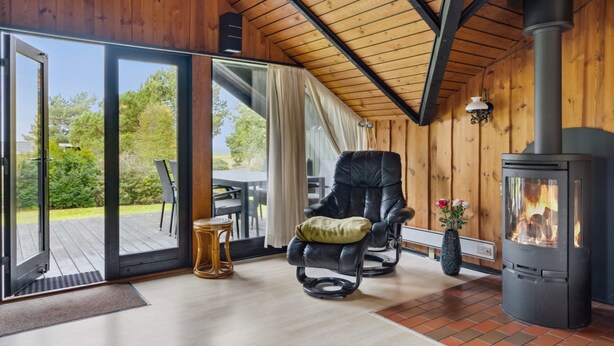 Una habitación acogedora con techo de madera, un sillón de cuero negro, una mesa y una estufa de leña.