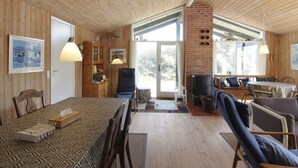 Un intérieur de chalet chaleureux avec un coin repas, une cheminée et une grande fenêtre.
