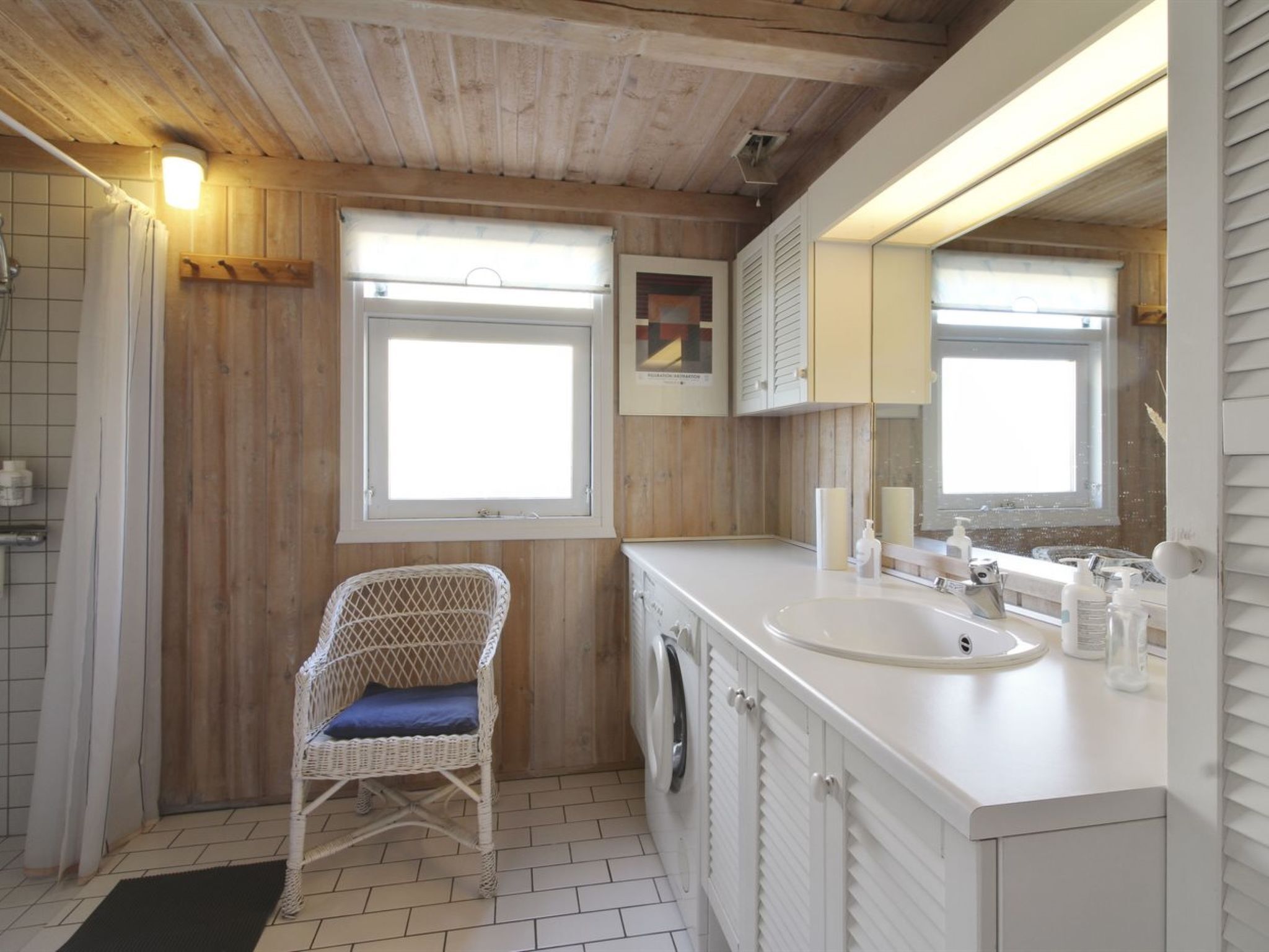 A bathroom with a wooden ceiling, a white sink, a wicker chair, and a mirror.