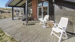 Une maison moderne dotée d’une terrasse en bois, d’un espace salon extérieur et d’une porte vitrée donnant sur un patio.
