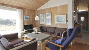 Un salon chaleureux avec un plafond en bois, un canapé, un fauteuil, un téléviseur et des œuvres d’art encadrées accrochées au mur.