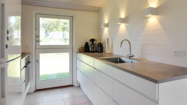 A modern kitchen with white cabinetry, a large window, and built-in lighting.
