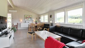 A spacious living area with a dining table, a black leather sofa, and a kitchen area with a white countertop and cabinets.