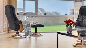 A modern living room with a large window, a black leather chair, a small table, and a potted plant.