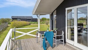 A modern house with a deck, large windows, and a view of the sea.