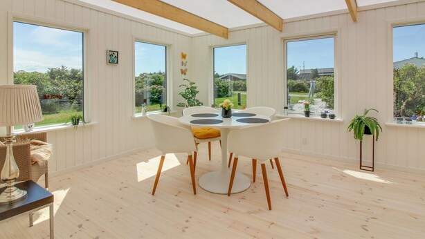 Une salle à manger lumineuse avec un plafond en bois, de grandes fenêtres et une vue sur l’extérieur.