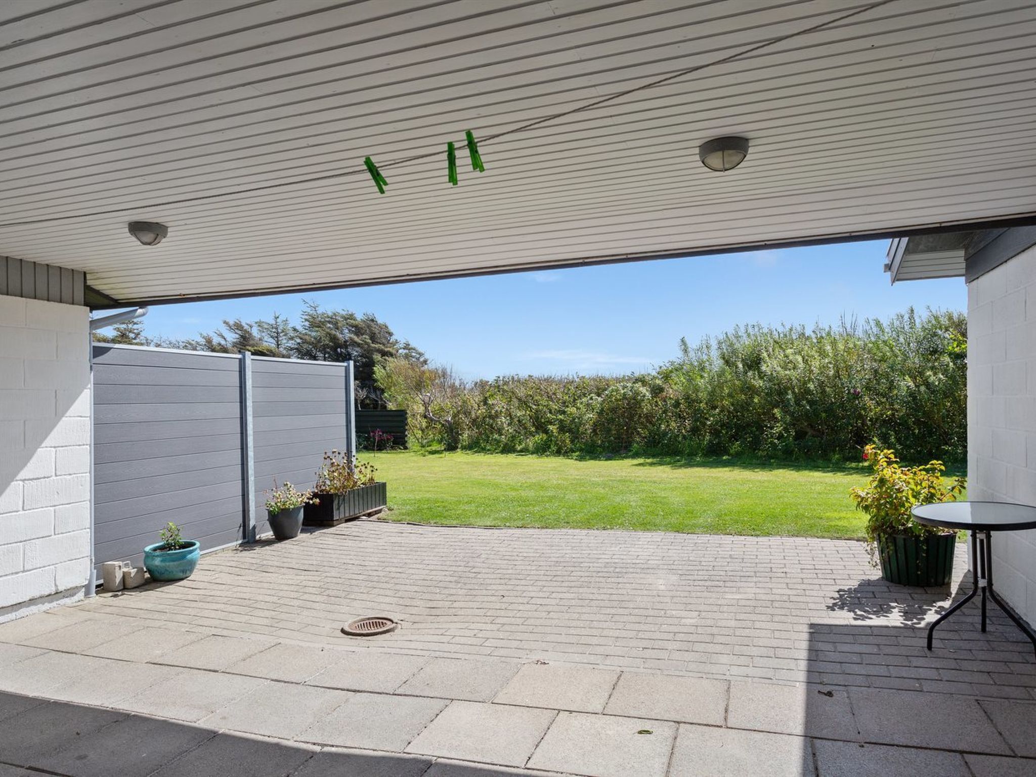 Een overdekt terras met een stenen vloer, een kleine tafel en potplanten.