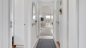 Un couloir blanc avec un plancher en bois, un tapis et une porte donnant sur une pièce avec vue.