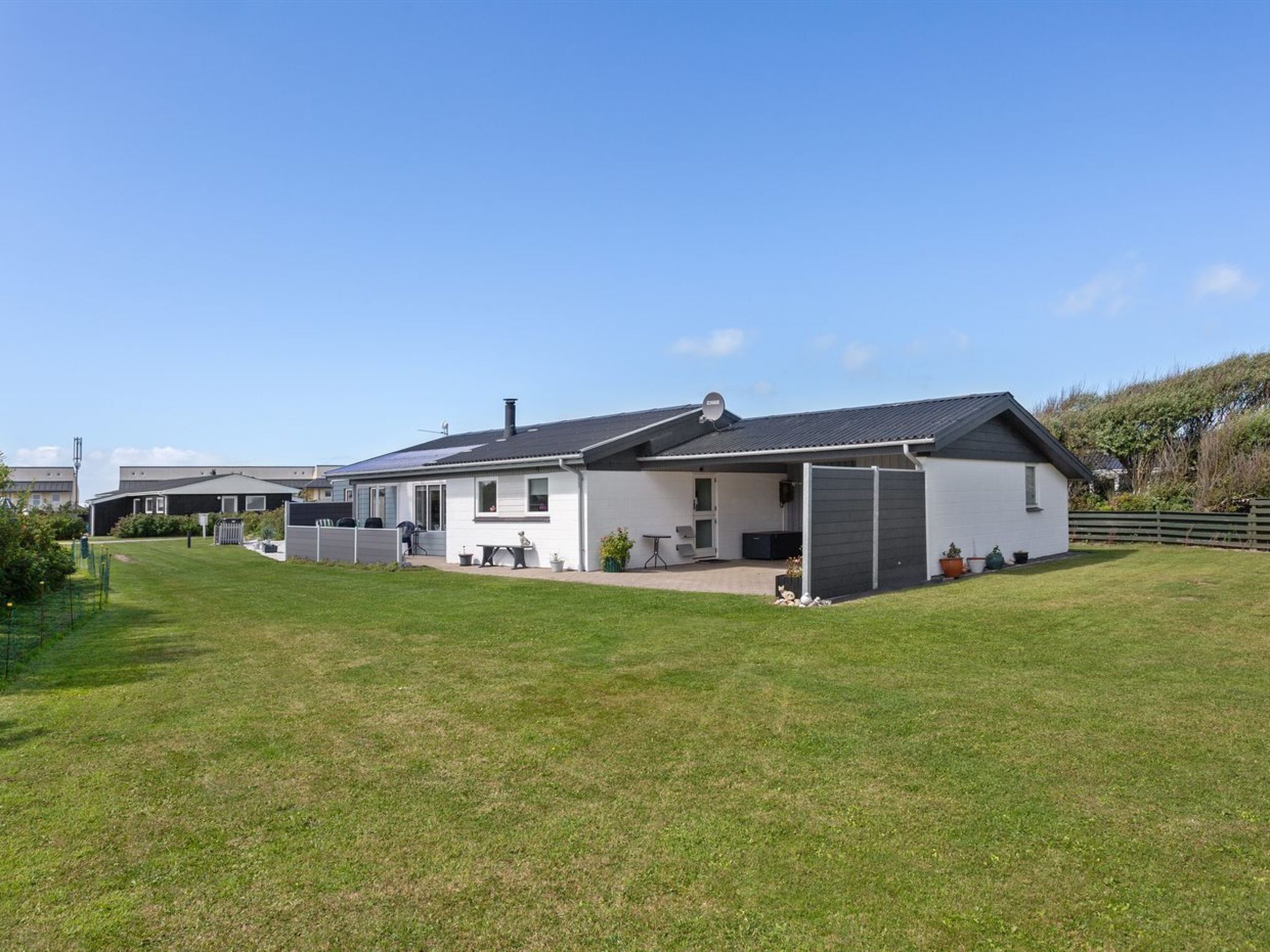 A single-story house with a covered patio, a fenced yard, and a satellite dish.