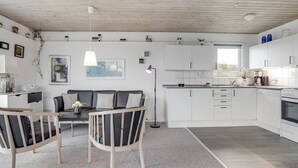 Une cuisine moderne avec des meubles blancs, un coin repas comprenant un canapé et des chaises, et une grande fenêtre laissant entrer la lumière naturelle.