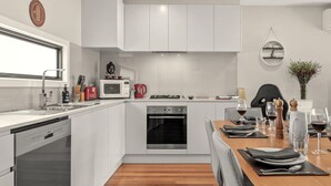 A modern kitchen with white cabinetry, a built-in oven, and a dining area with a wooden table set for two. - StayCentral - Thornbury Townhouse (Thornbury)