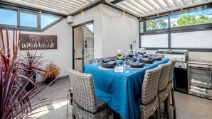 An outdoor dining area with a blue tablecloth, wicker chairs, and a grill station. - StayCentral - Thornbury Townhouse (Thornbury)