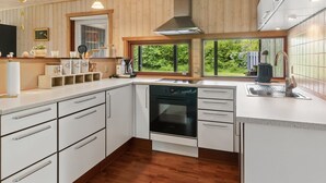 A modern kitchen with wooden paneling, a built-in oven, and a large window offering a view of greenery. - "Linda" - 600m from the sea by Interhome (Sjællands Odde)