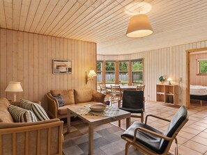 Una habitación acogedora con paredes y techo de madera, un rincón de comedor con mesa y sillas, un sofá y una cama.