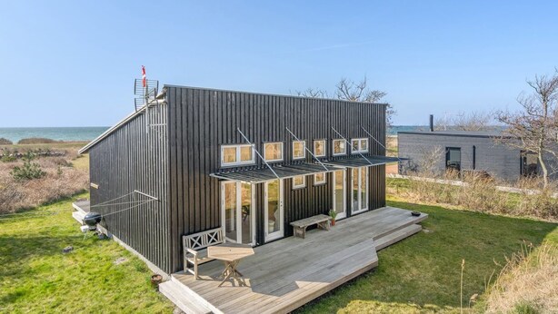 Une maison moderne à deux étages, dotée d’une terrasse, de grandes fenêtres et offrant une vue sur la mer.