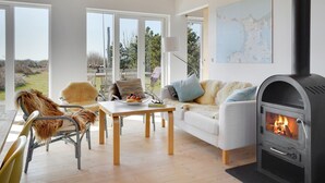 Un salon moderne doté d’une cheminée, d’un coin repas avec une table et des chaises, et de grandes fenêtres offrant une vue sur l’extérieur.