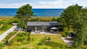Una casa moderna con un patio, un coche aparcado delante y vista al océano.
