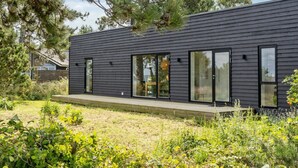 Una casa moderna con fachada oscura, ventanas amplias y una terraza de madera.