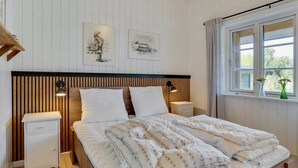 Un lit bien fait, avec une couette à motifs, deux tables de chevet avec des lampes, une tête de lit en bois et deux œuvres d’art accrochées au mur.
