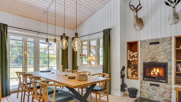 Un coin repas chaleureux avec une table et des chaises en bois, une cheminée en pierre et des têtes d’animaux décoratives accrochées au mur.