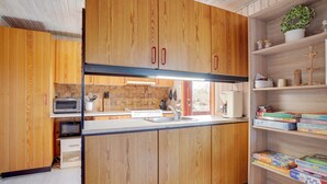 Eine Küche mit Holzausbau, einer Mikrowelle, einer Kaffeemaschine und einem Bücherregal mit Knobelbüchern.