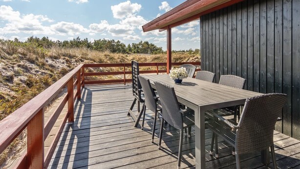 Eine Holzterrasse mit Tisch und Stühlen mit Blick auf einen Strand und Dünen.