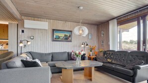 Ein modernes Wohnzimmer mit Holzboden, grauen Sofas, einem Couchtisch und einem großen Fenster mit Blick ins Freie.