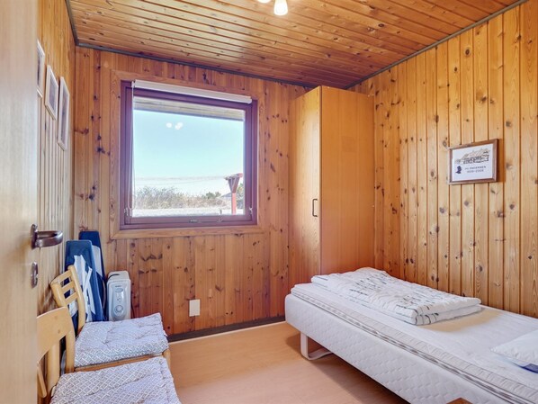 A wooden cabin room with a single bed, a window, and a framed certificate on the wall.