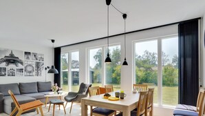 A modern living room with a dining area, large windows, and a view of the outdoors.