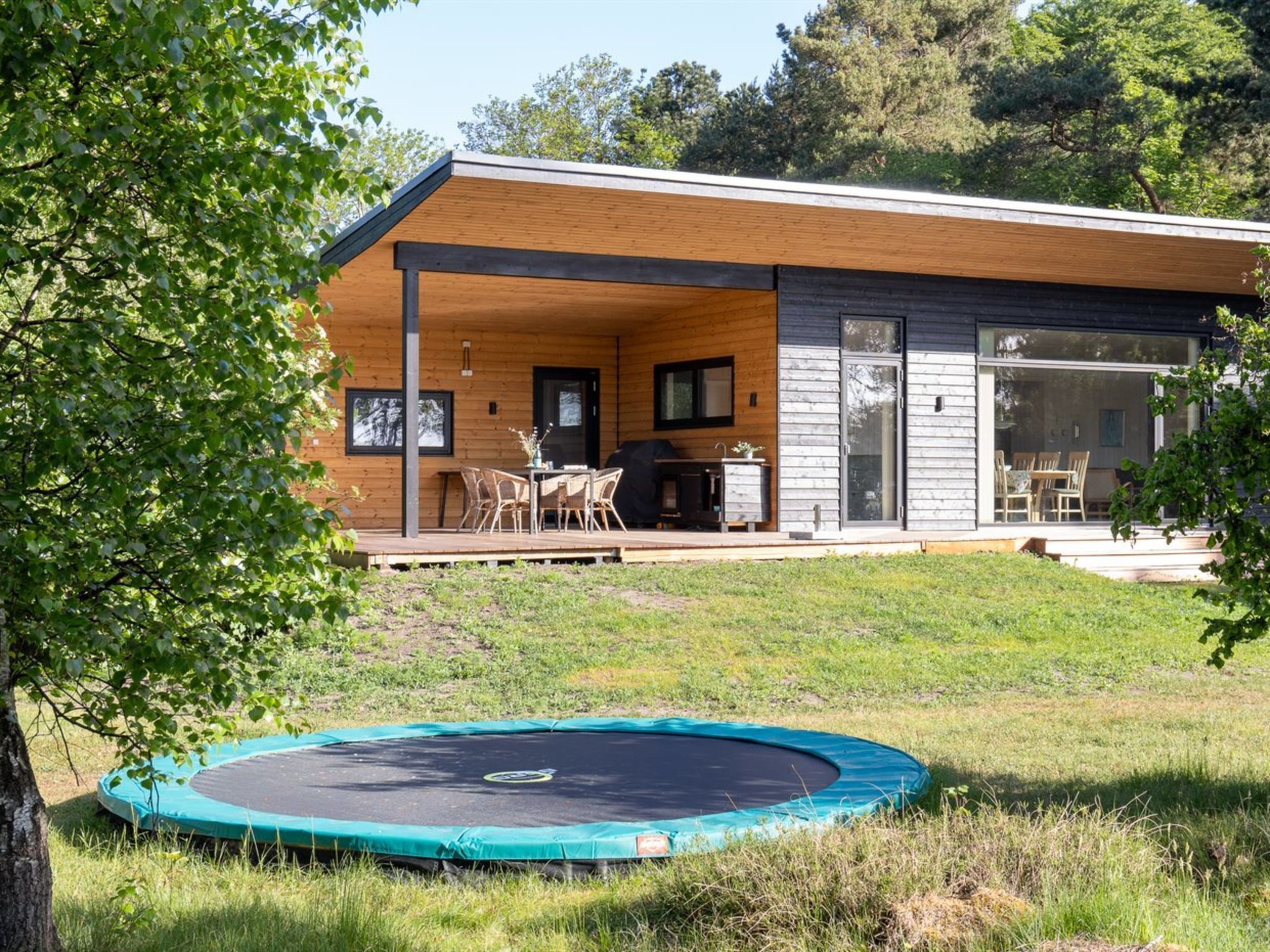 Une maison moderne dotée d’une terrasse en bois et d’un trampoline dans le jardin.