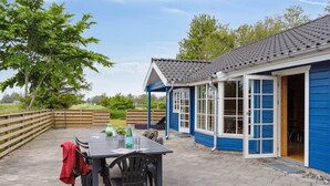 A patio with a table and chairs, a blue building with a tiled roof, and a wooden fence.