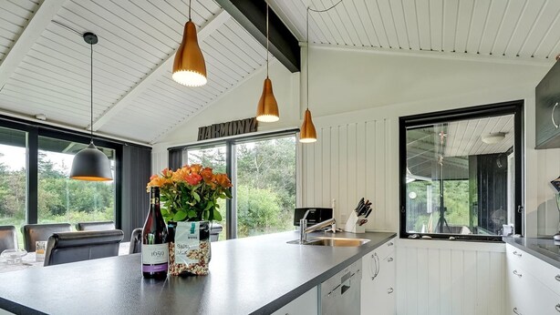 Une cuisine moderne dotée d’un grand îlot central, de luminaires suspendus et offrant une vue sur l’extérieur.