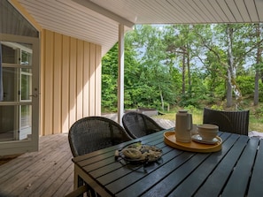 A wooden deck with a table set for two, surrounded by chairs, and a view of a forested area.