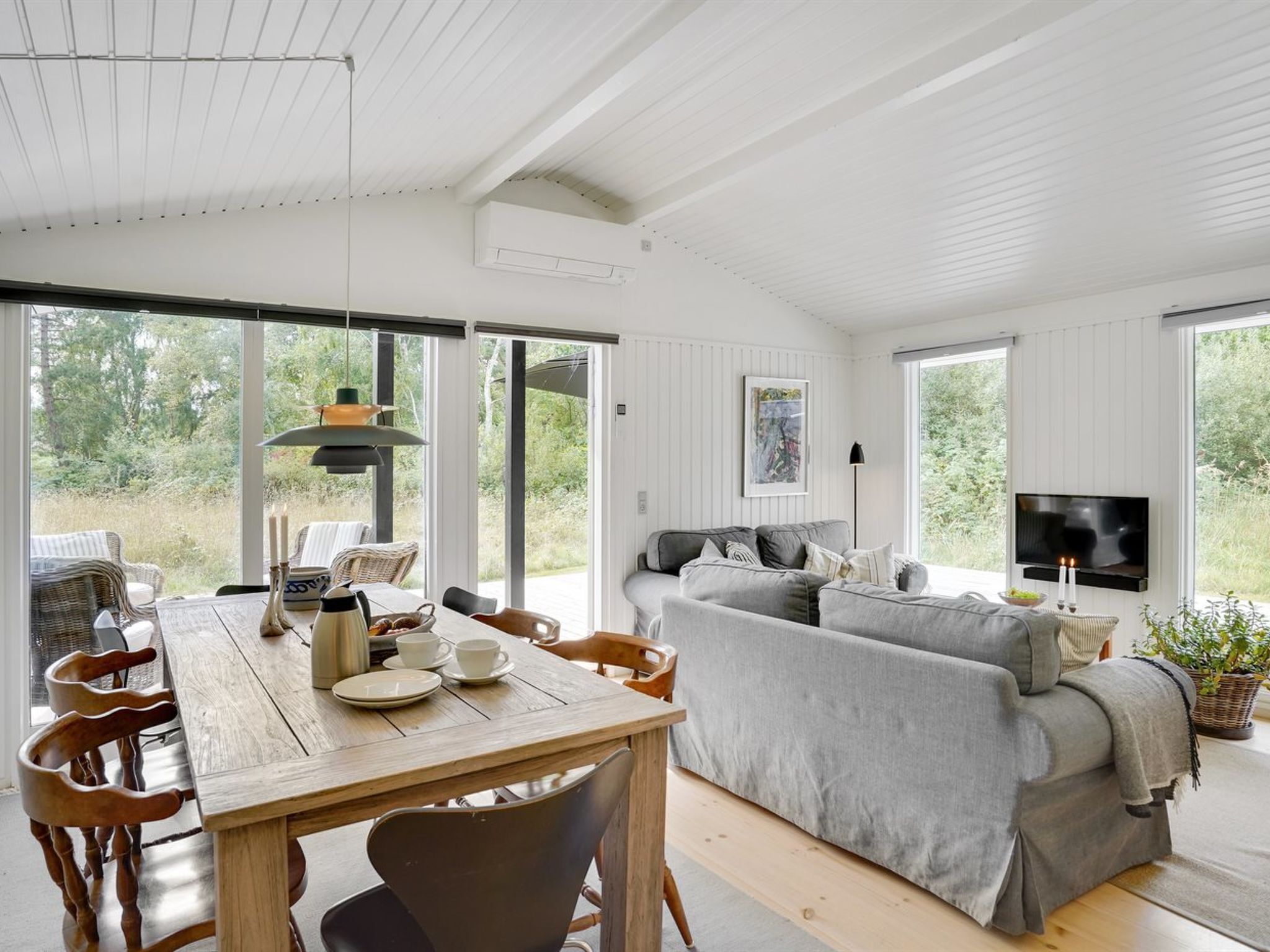 Un vaste espace de vie comprenant une table à manger en bois, un canapé gris et un téléviseur fixé au mur.