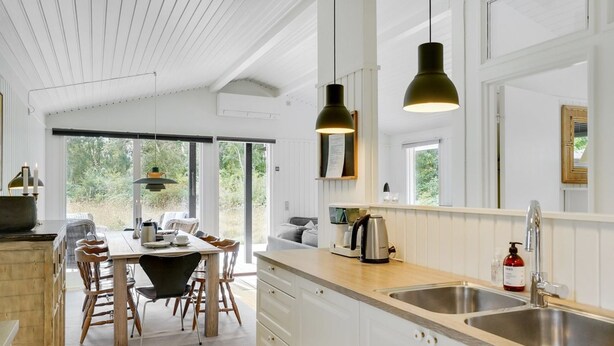 A modern kitchen with white cabinetry, a wooden dining table, and pendant lights.