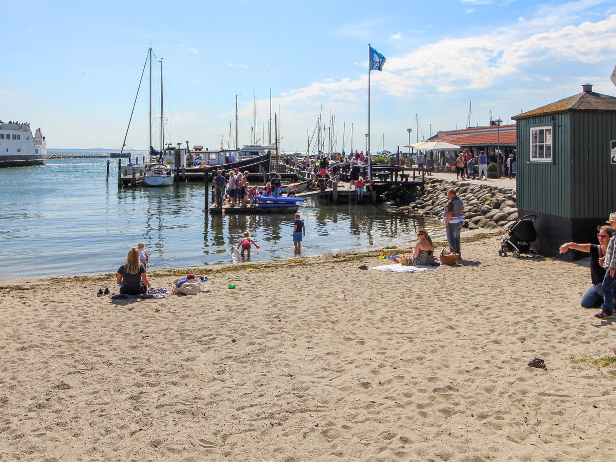 Une plage avec des gens, des bateaux et un petit bâtiment.