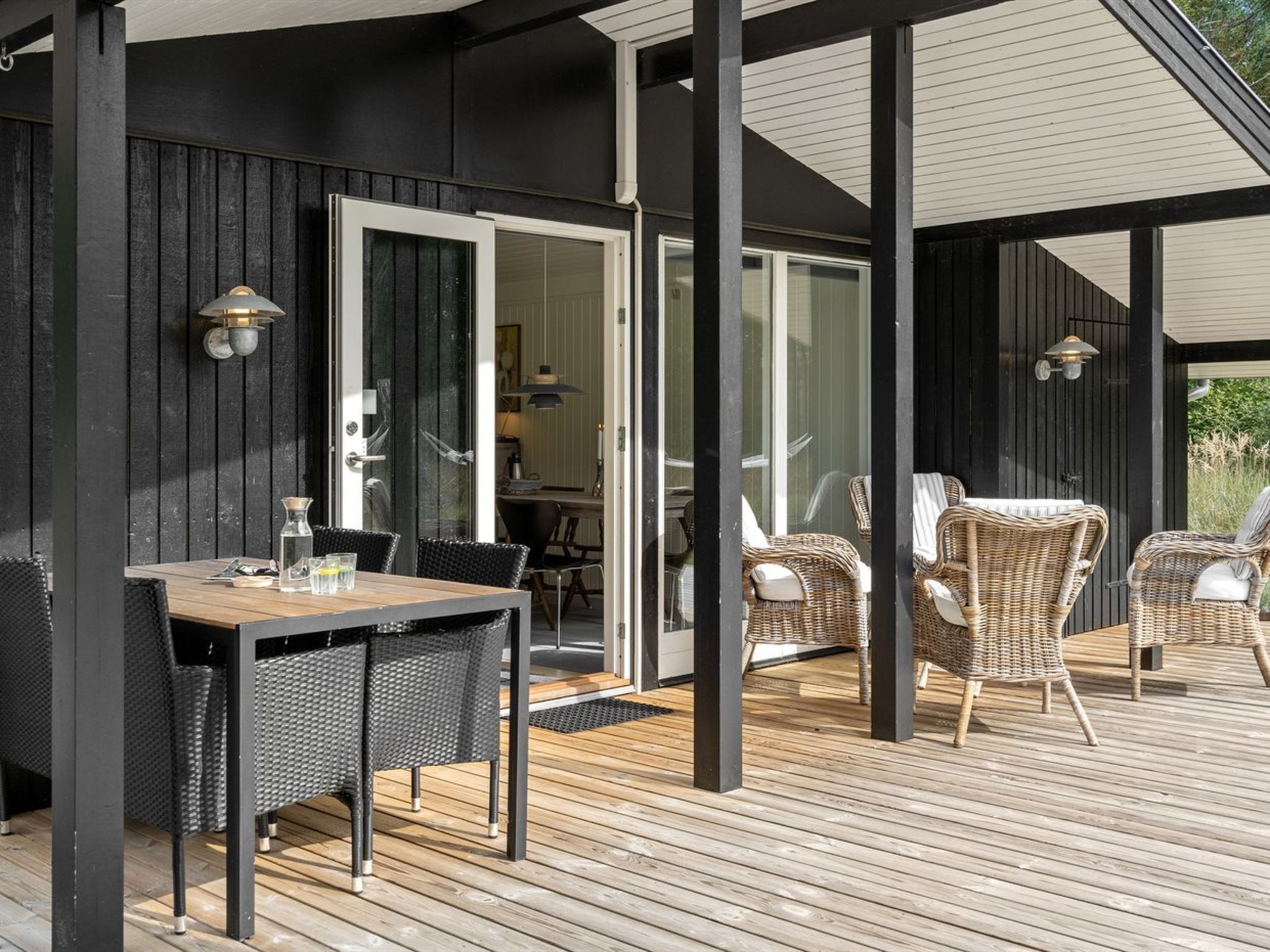 Une terrasse extérieure avec une table et des chaises en bois, une porte vitrée donnant sur un espace intérieur et un mur extérieur noir.