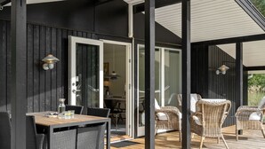 An outdoor deck with a wooden table and chairs, a glass door leading to an interior space, and a black exterior wall.