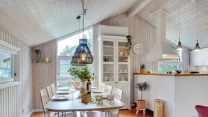 A dining area with a wooden table set for four, surrounded by white chairs. A hanging light fixture and a clock on the wall are visible. - "Elayne" - 3km from the sea by Interhome (Blokhus)