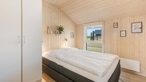 Een slaapkamer met een bed, houten wanden, een kledingkast en een raam met uitzicht.