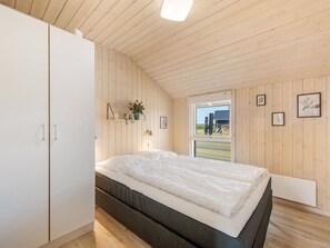 Une chambre à coucher avec un lit, des murs en bois, une armoire et une fenêtre donnant sur un beau paysage.