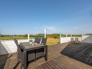 Una terraza con mesa y sillas, con vista a un área verde con una valla blanca y una chimenea.