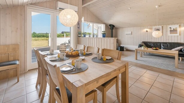 Een ruime eethoek met een houten tafel gedekt voor het ontbijt, een bank in de woonkamer en uitzicht op de omgeving.