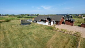 Een woonhuis met een groot gazon, een trampoline en een huis met een schuin dak.