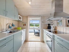 Una cocina moderna con armarios de madera clara, un lavamanos de acero inoxidable y vistas al exterior.