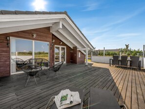 A covered outdoor deck with wooden flooring, metal chairs, and a table with a magazine.